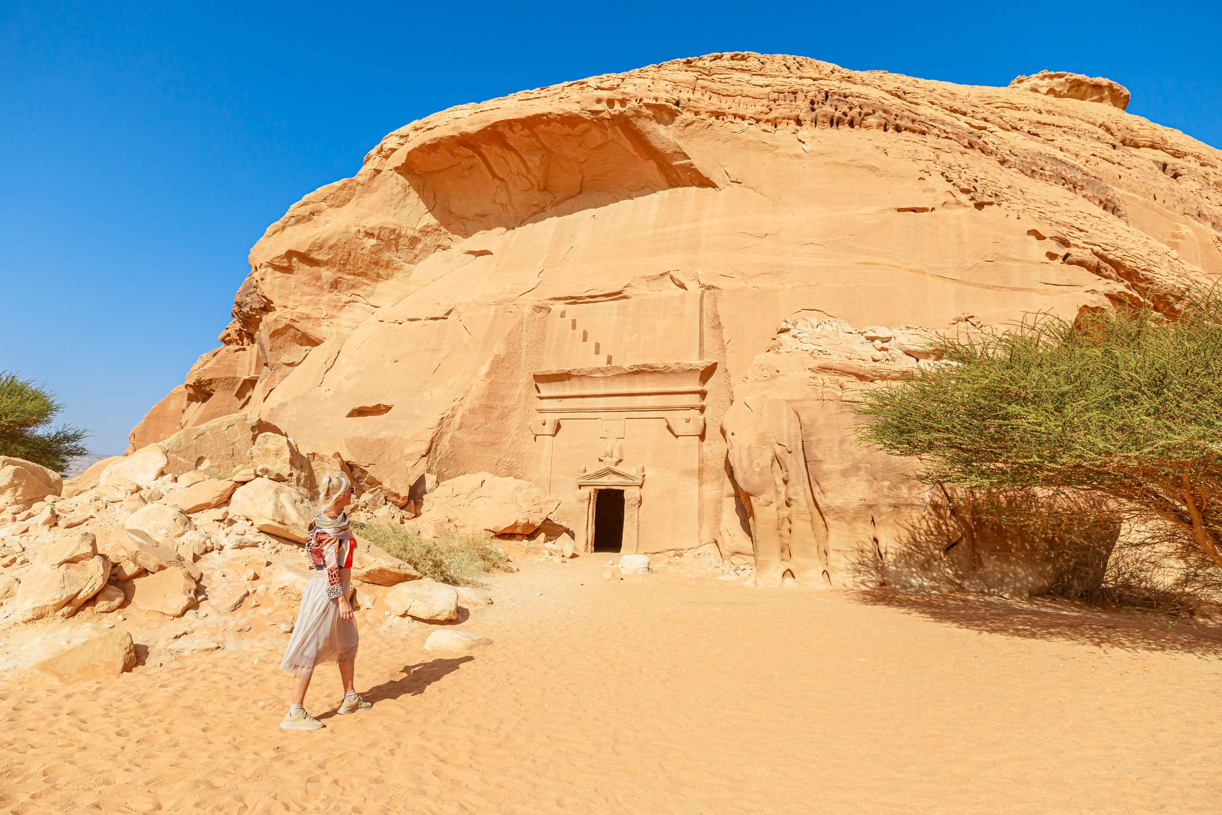 Blonde Tourist Walking In The Desert Next To Of Jabal Albanat And Giant Rock Cut Tomb 